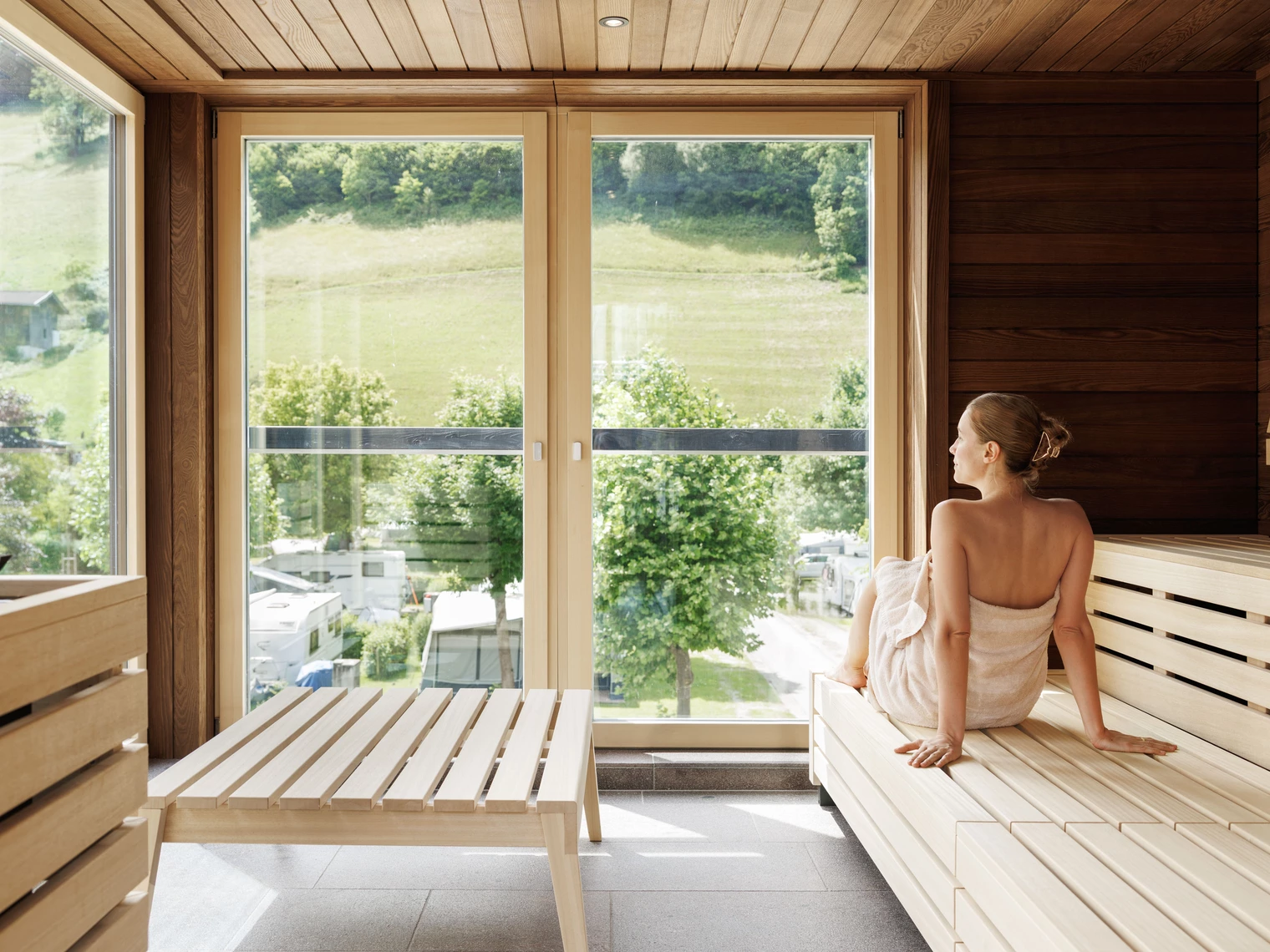 Frau sitzt mit einem Handtuch eingewickelt in einer Sauna.