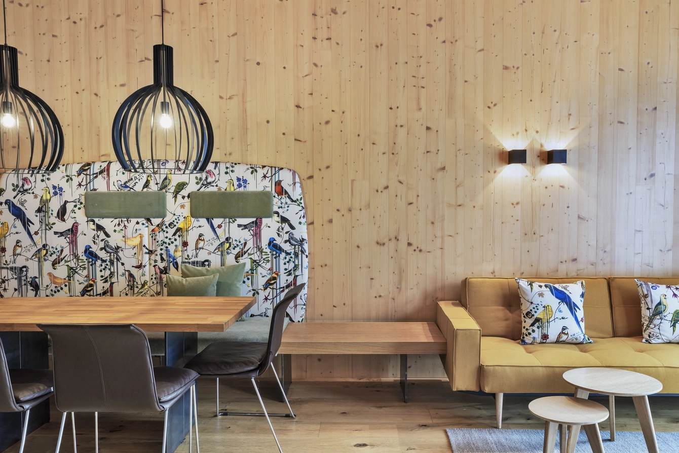 Apartment Sonnwend ©Natürlich HELL Camping & Aparthotel Der Essbereich des Sonnwend Apartments mit einem Holztisch neben dem sich ein gelbes Sofa mit bunten Dekokissen befindet.