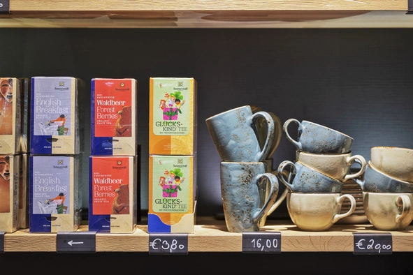 Ein Regal des Shops mit verschiedenen Teesorten wo sich rechts daneben blaue und braune Tassen befinden.