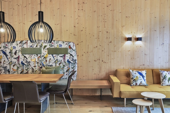Apartment Sonnwend ©Natürlich HELL Camping & Aparthotel Der Essbereich des Sonnwend Apartments mit einem Holztisch neben dem sich ein gelbes Sofa mit bunten Dekokissen befindet.