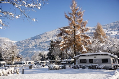 Wohnwagen auf einem verschneiten Campingplatz mit Bergen im Hintergrund.
