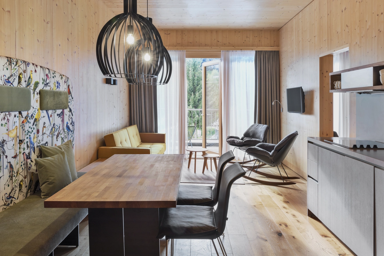 Apartment Sonnwend ©Natürlich HELL Camping & Aparthotel Der hell beleuchtete Wohn- und Essbereich des Sonnwend Apartments mit einem hölzernen Esstisch und einem modernen Sitzbankdesign.