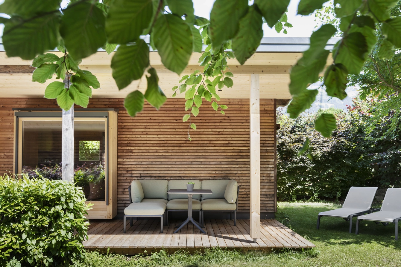 Überdachte Terrasse Garten Lodge ©Natürlich HELL Camping & Aparthotel Die überdachte Terrasse der Garten Lodge in Holzoptik, einer Sitzecke mit Tisch und zwei Liegen im Gras.