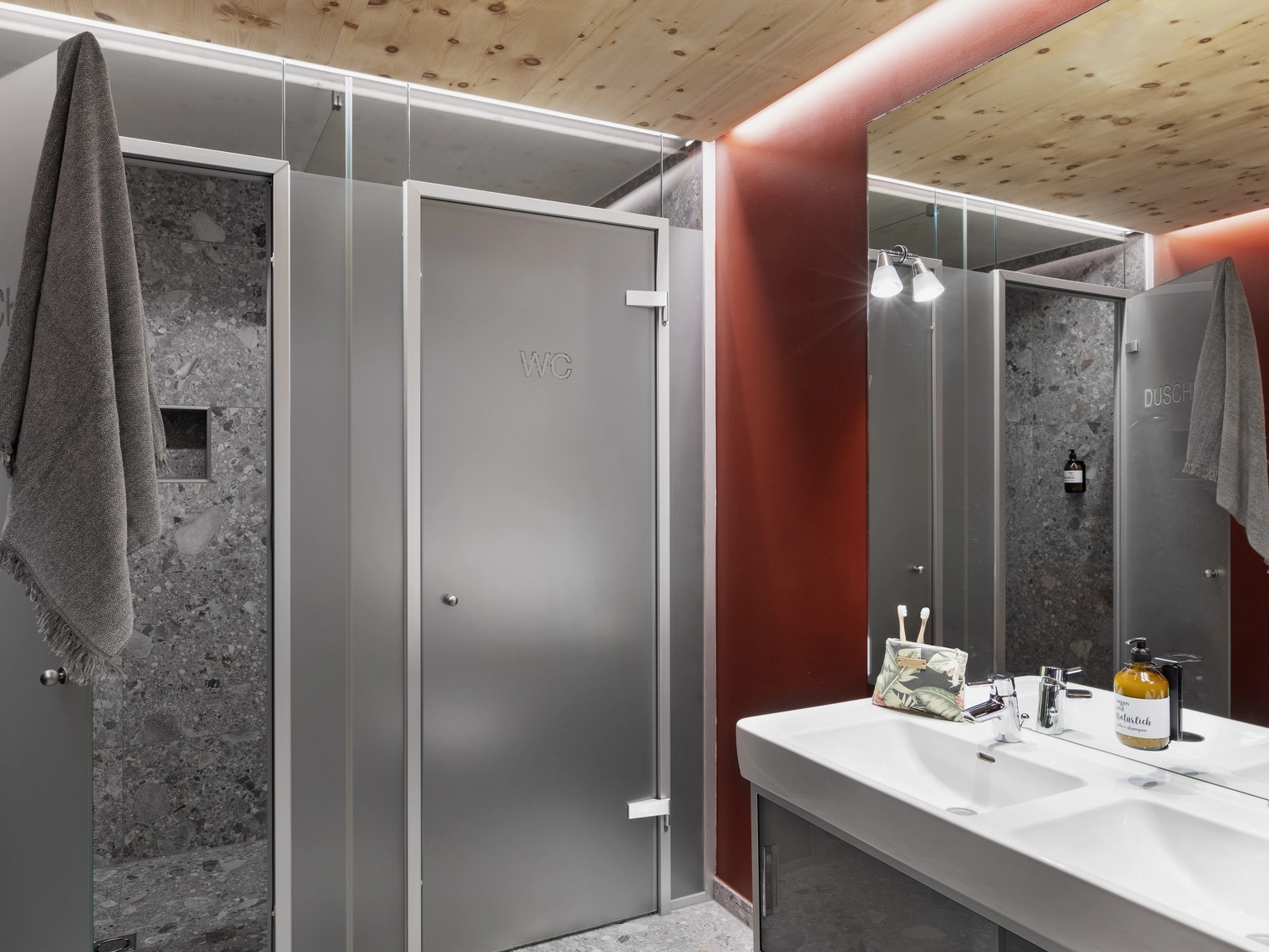 Ein Privatbad des Campingplatzes in dunklen Farben wie rot und grau, zwei Waschbecken, zwei getrennten Türen für Toilette und Dusche.