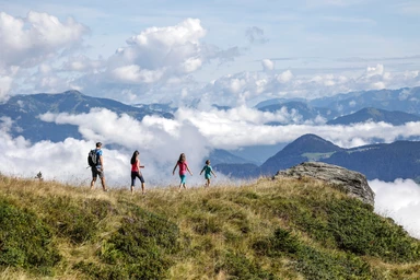 Eine Familie auf einem grasigen Berghang mit Aussicht auf die Wolken.