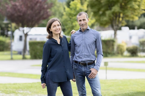 Die Geschäftsführung des Natürlich Hell arm-in-arm mit dem Campingplatz im Hintergrund.