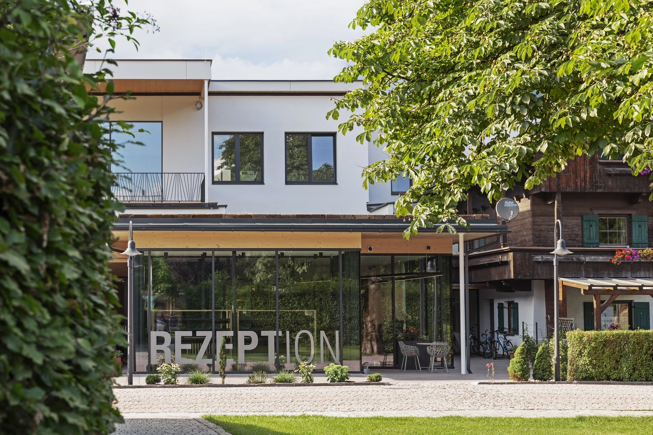 Rezeption außen ©Natürlich HELL Camping & Aparthotel Die Rezeption des Natürlich Hell untertags und von draußen betrachtet mit links einer Hecke und rechts einem Baum im Bild.