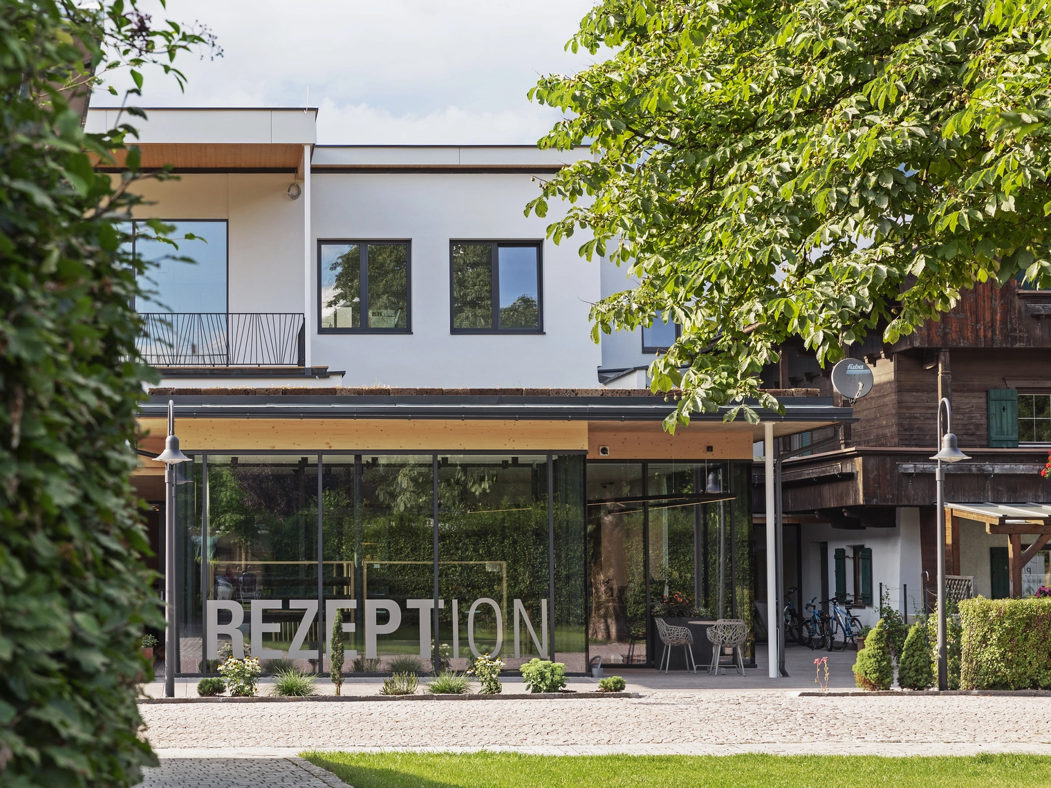 Die Rezeption des Natürlich Hell untertags und von draußen betrachtet mit links einer Hecke und rechts einem Baum im Bild.