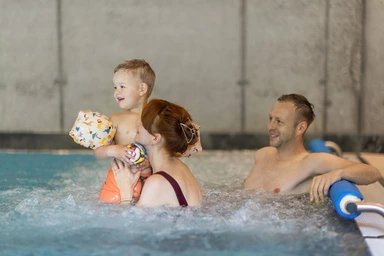 Zwei Erwachsene schwimmen mit ihrem Kind im Hallenbad