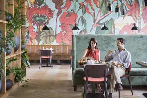 Zwei Personen die im Frühstücksraum des Camping & Aparthotels an einem fein gedeckten Tisch sitzen, und ihr Frühstück, als einzige im Raum, genießen.